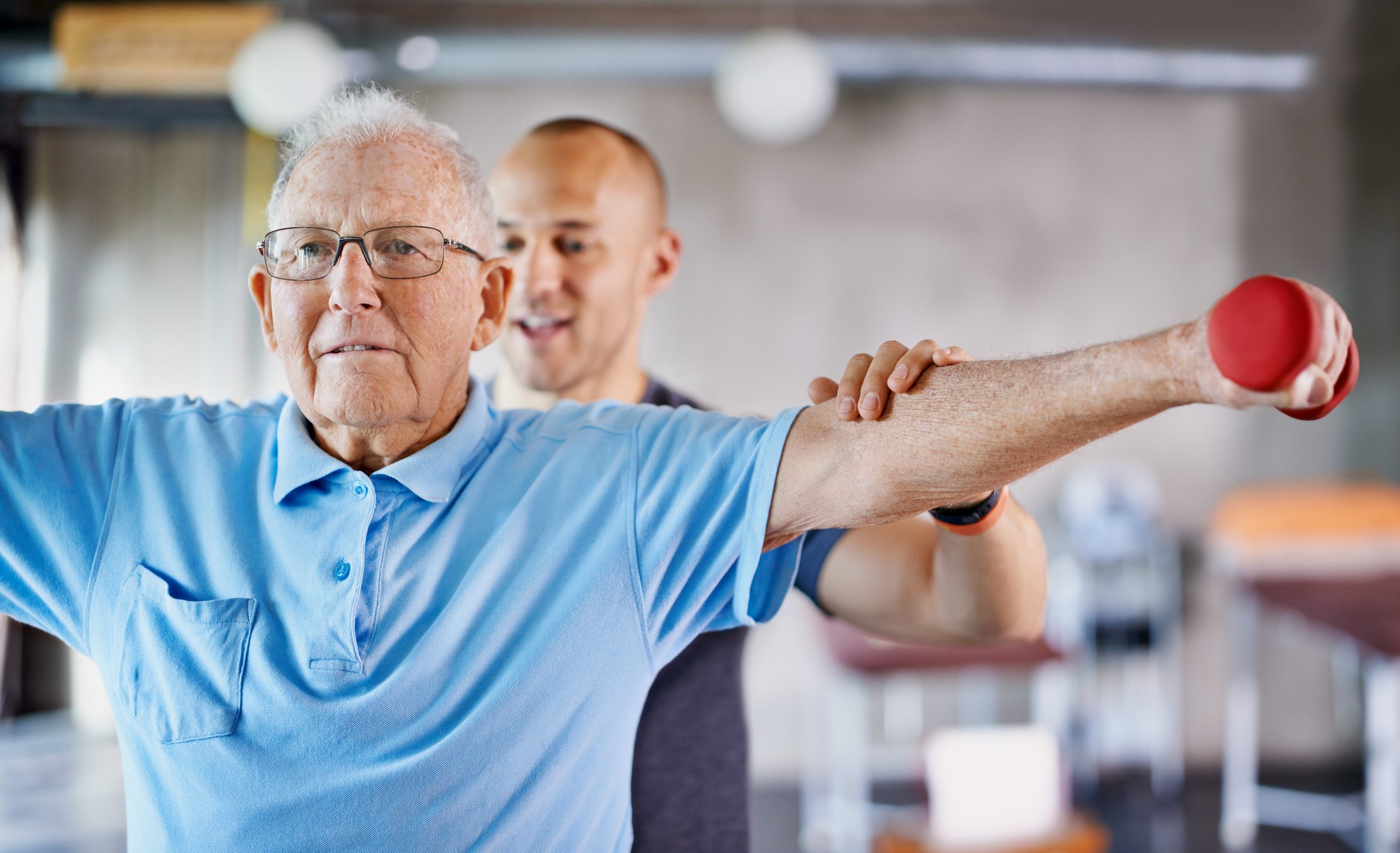 Ein Physiotherapeut unterstütze einen älteren Mann beim Training mit einer Hantel.